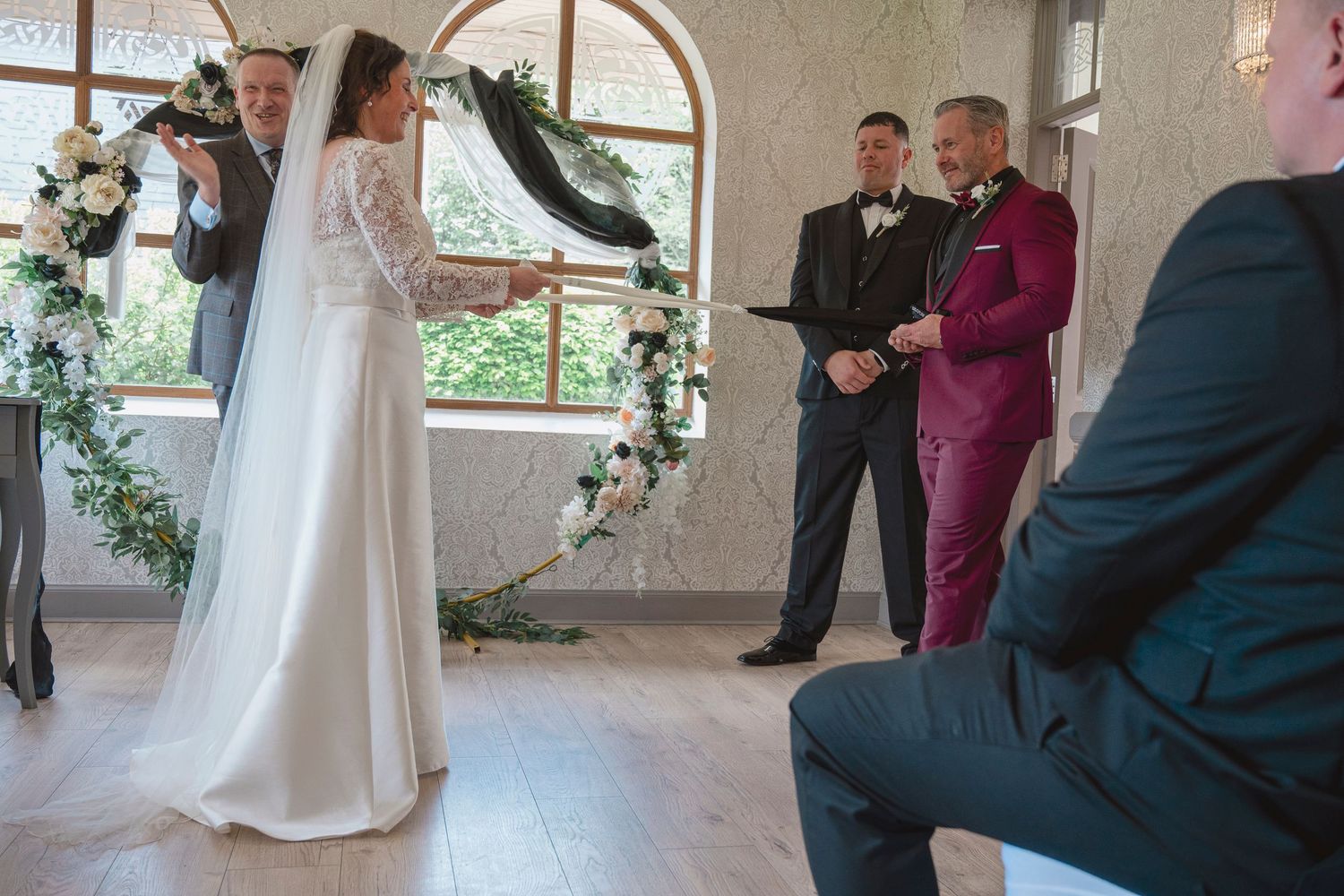 Bride and groom exchanging vows at elegant indoor wedding ceremony with floral arch and officiant.