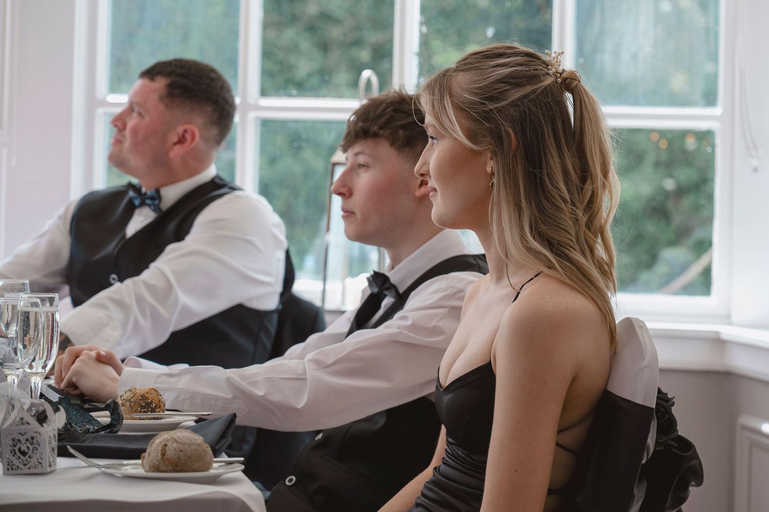 Guests in formal attire seated at a elegantly set table during a wedding reception indoors.