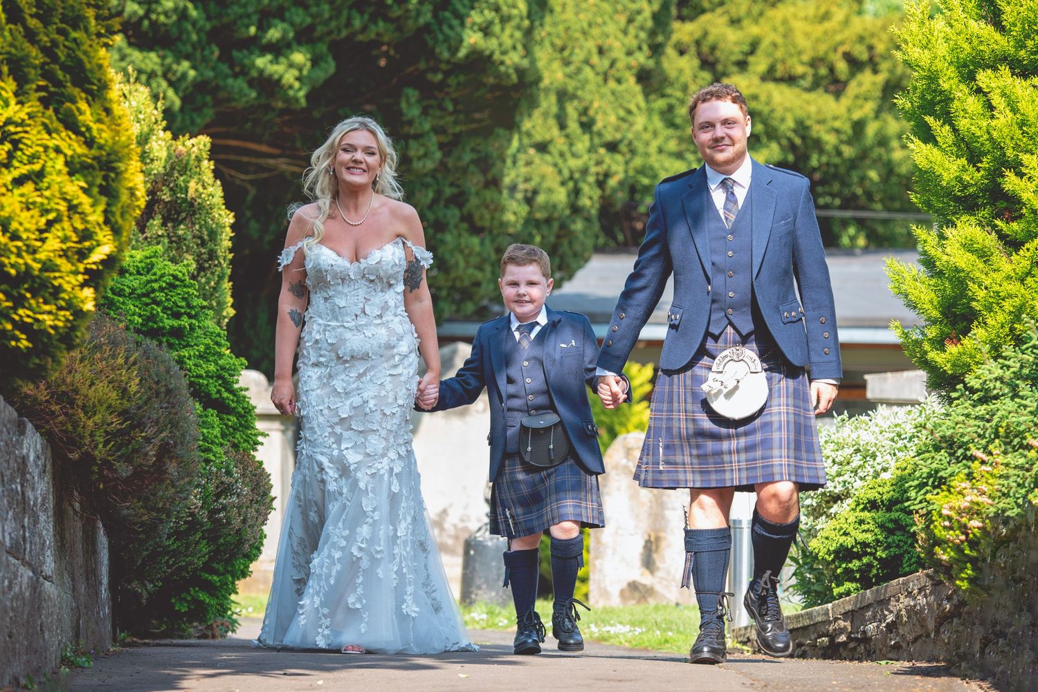 Wedding party walking through lush garden path on sunny day.