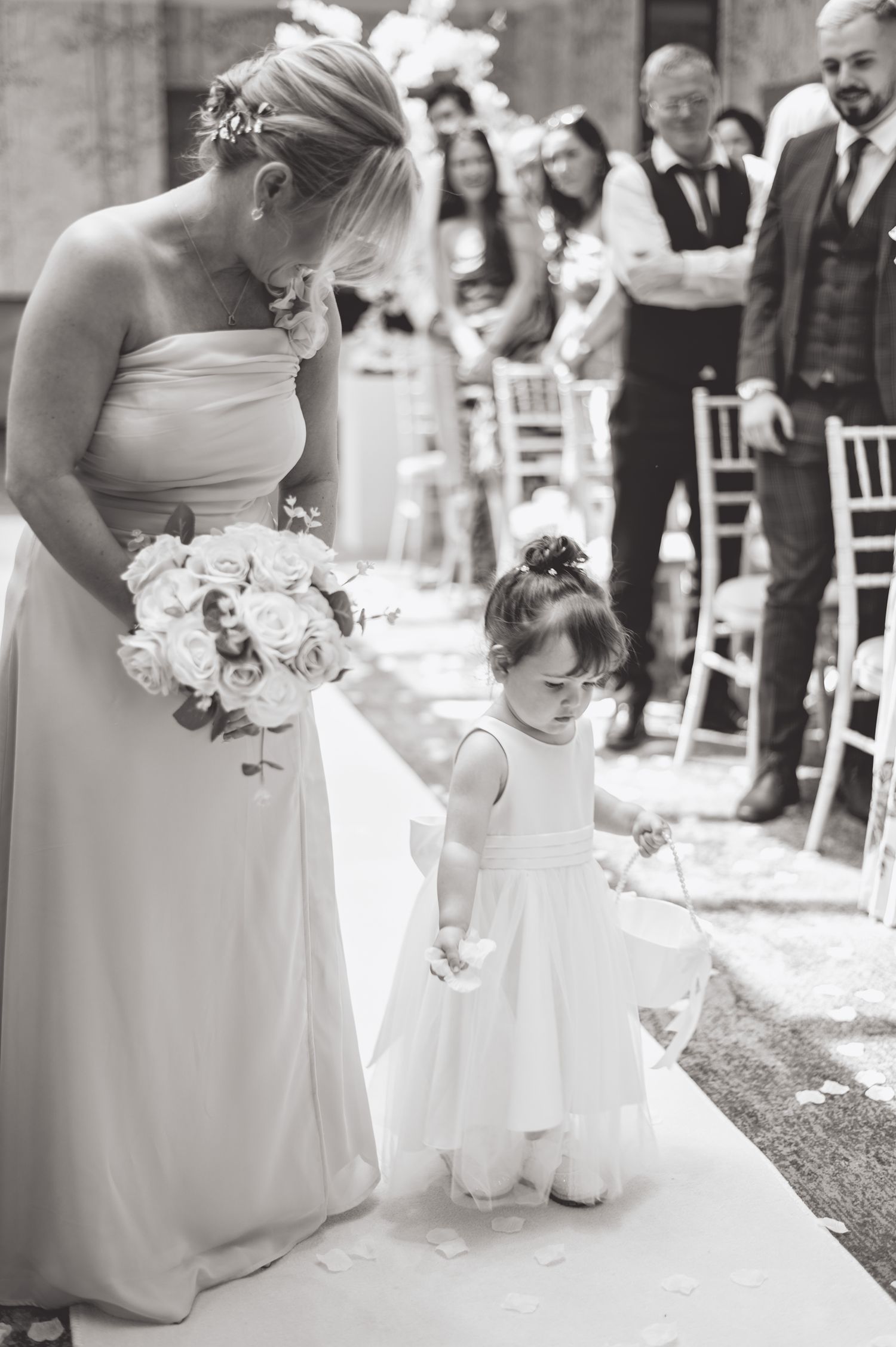 Black and white photo of attendants in formal wear standing on a white aisle runner at a wedding.