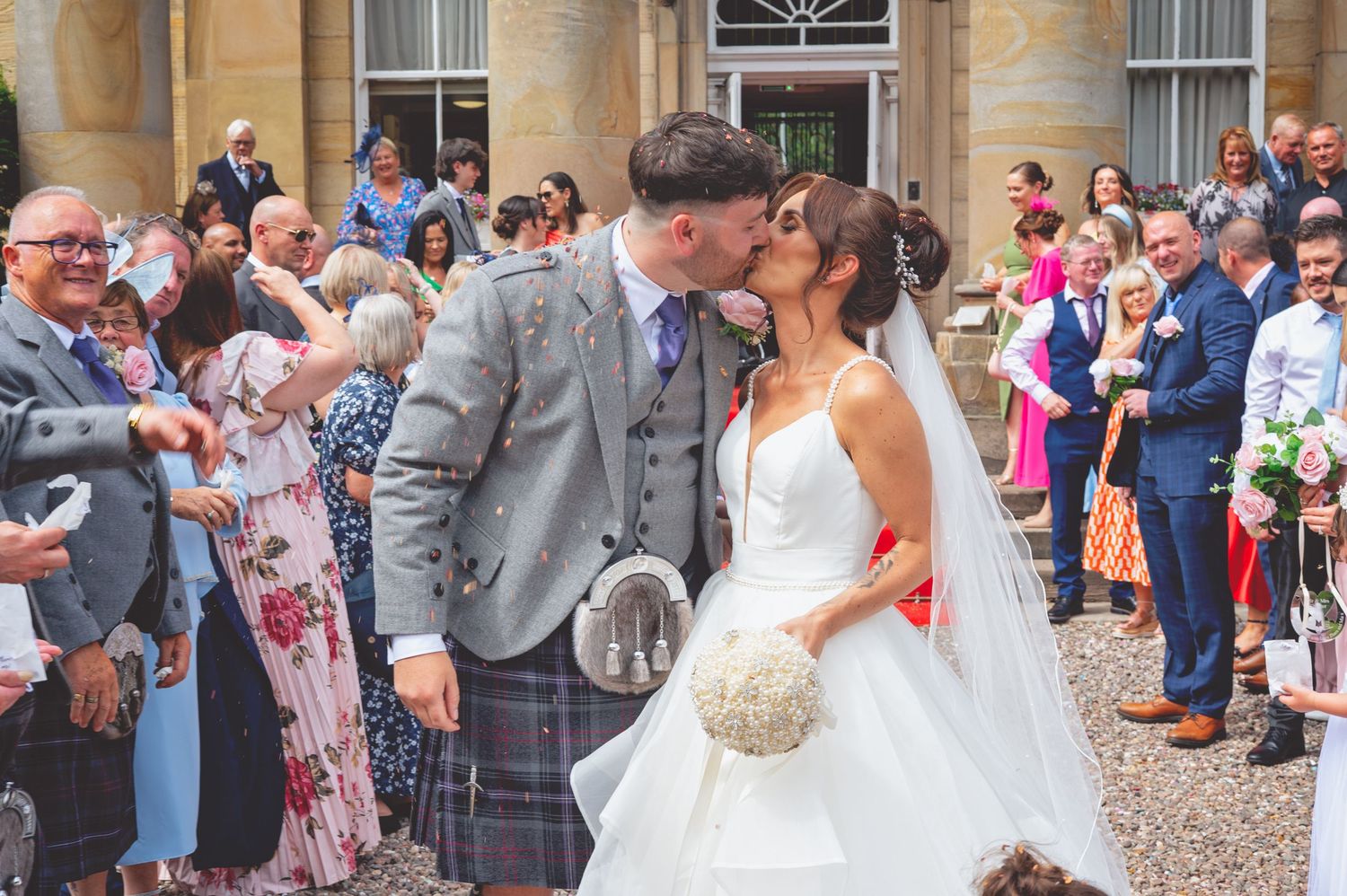 Joyful wedding celebration with guests cheering outside a stone venue.