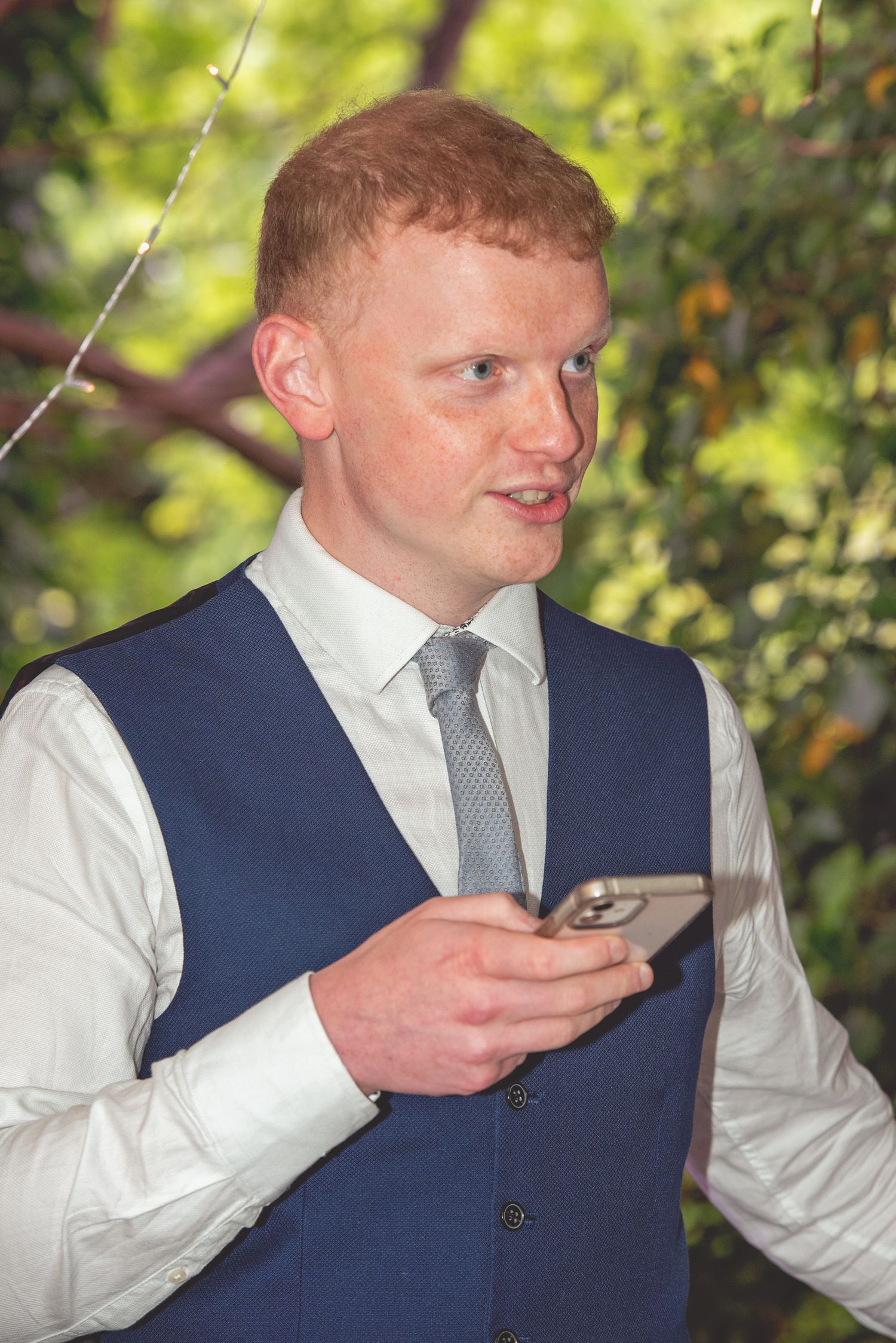 A guest in a navy waistcoat checks his phone during a wedding reception.