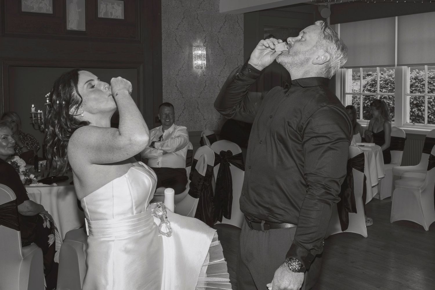 Bride and groom doing shots together at their wedding reception in black and white photo.
