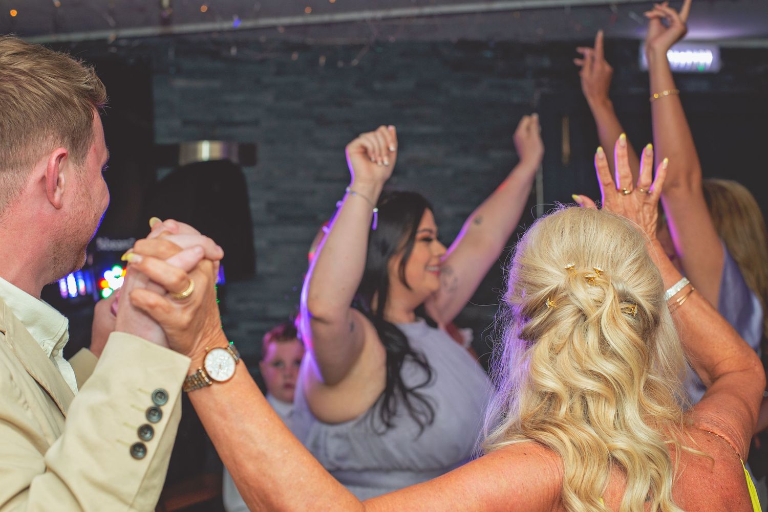 Wedding reception dance floor filled with celebrating guests under dim lighting.