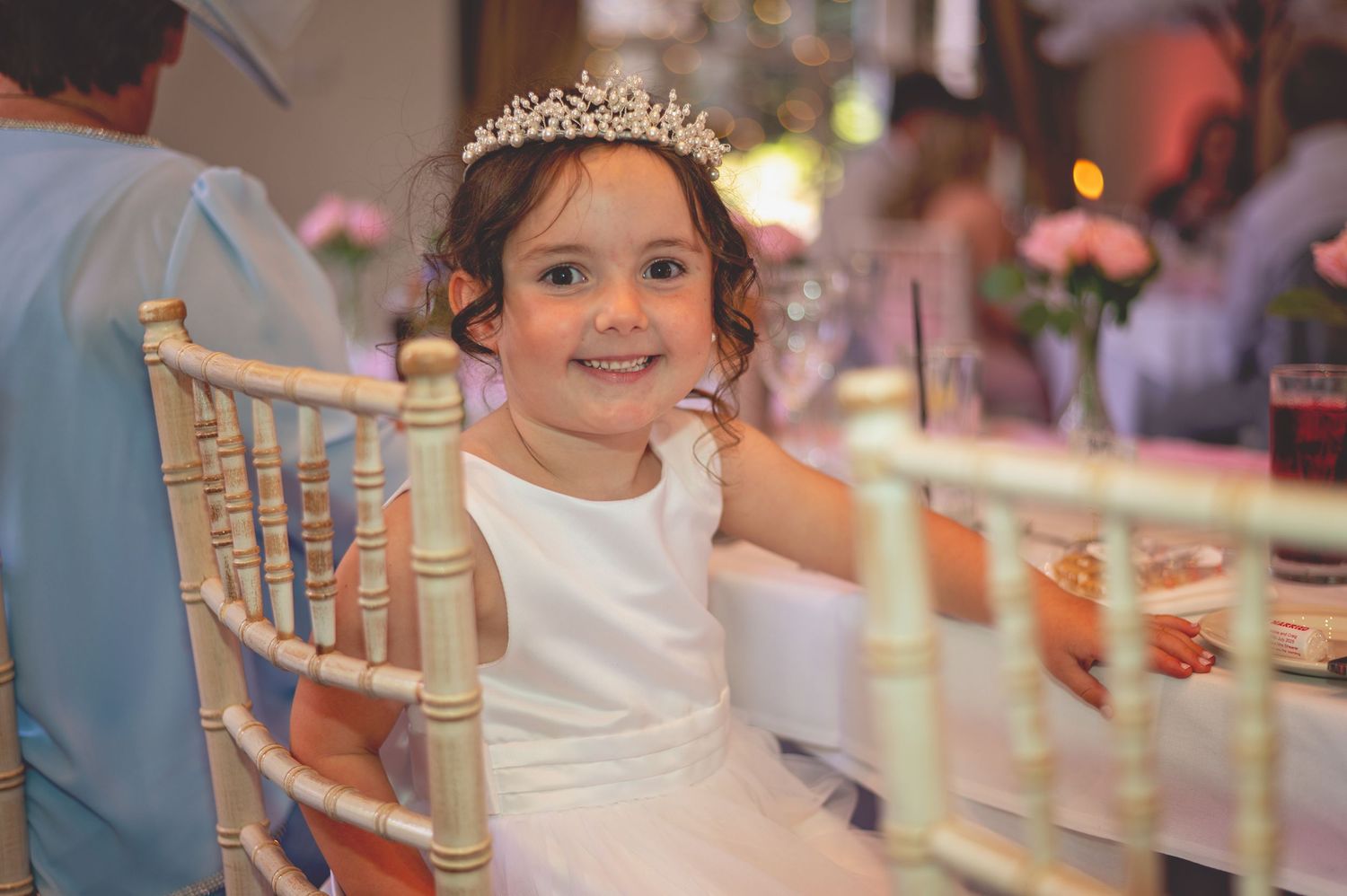 Young wedding guest in white dress sits at decorated reception table.