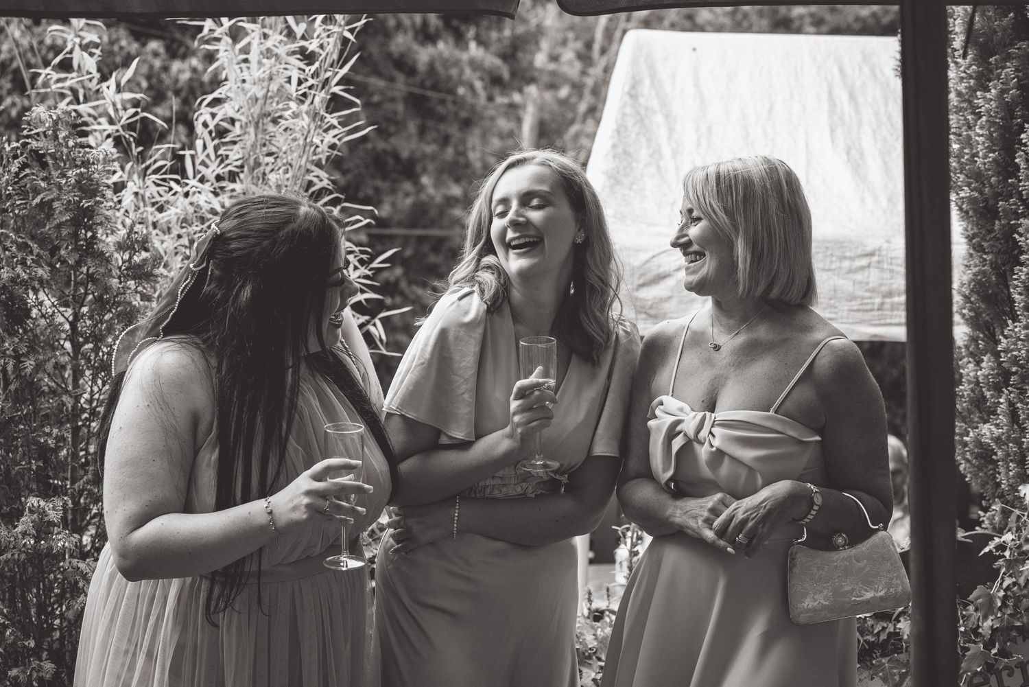 Black and white photo of three wedding guests sharing a joyful moment outdoors.