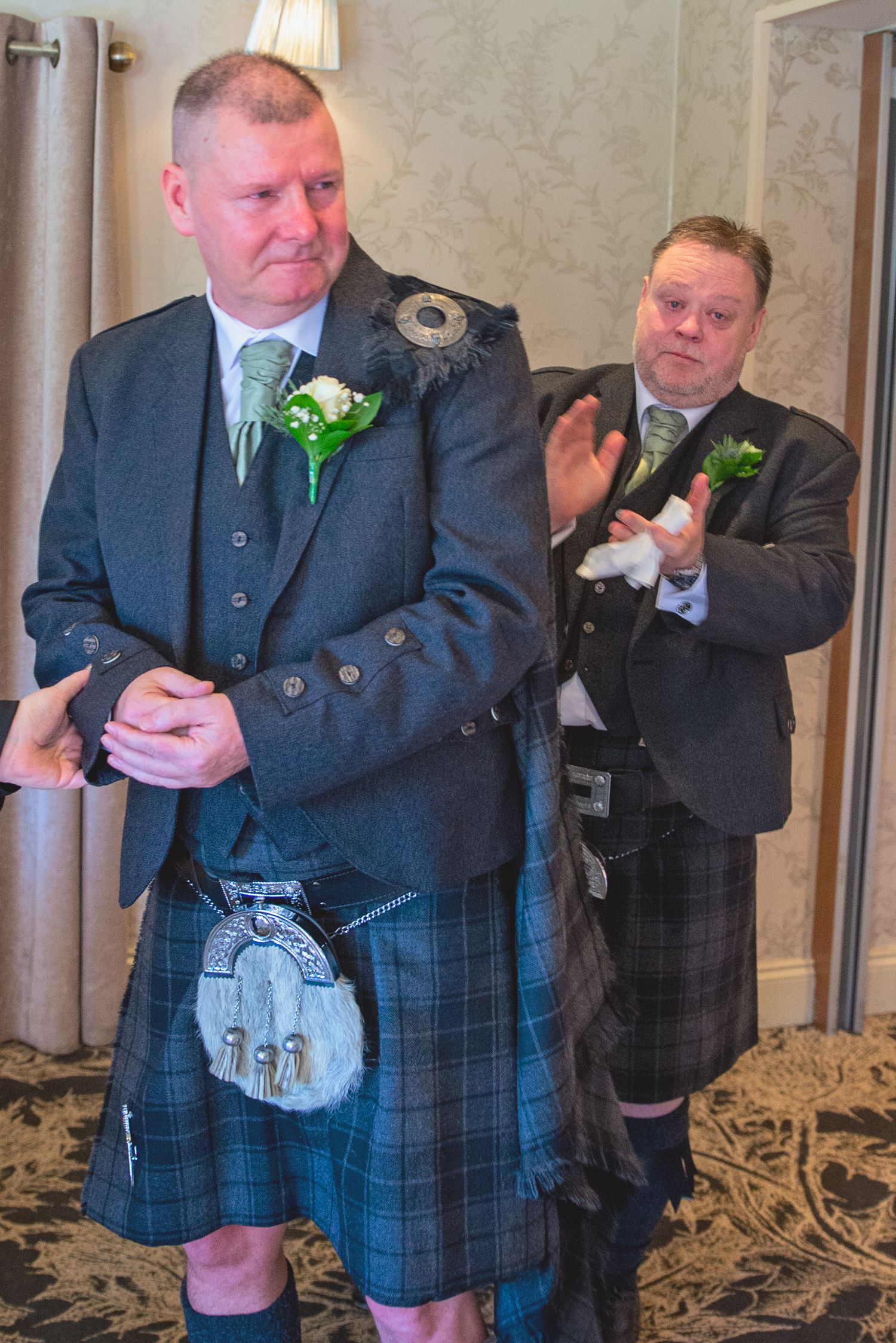 Groomsmen in traditional Scottish kilts and jackets pose together at a formal event.