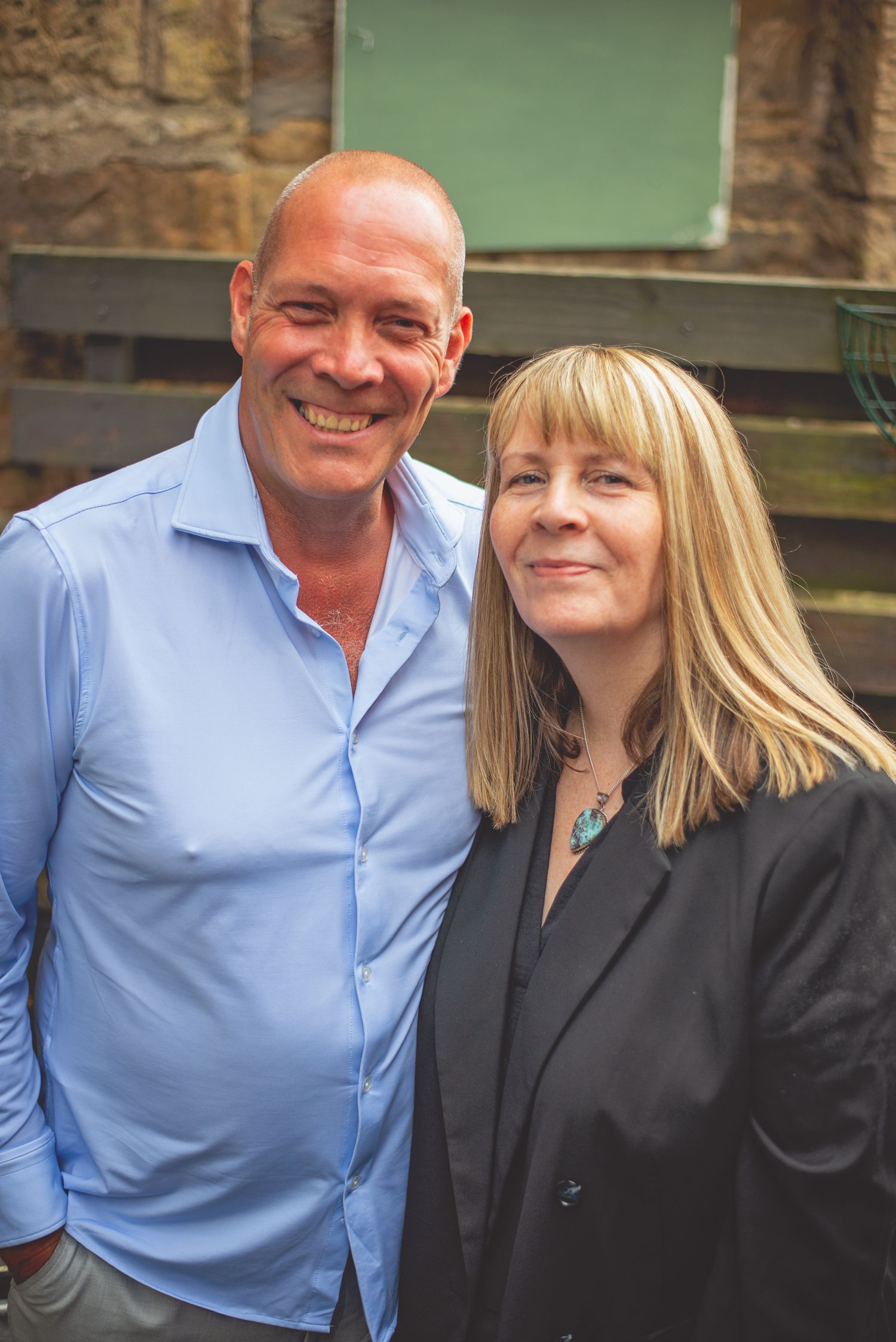 A couple poses together outdoors against a stone wall background.