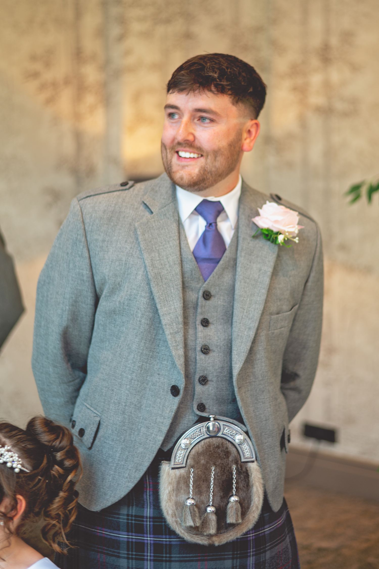 Groom wearing a traditional grey suit with Scottish kilt and sporran at a wedding.