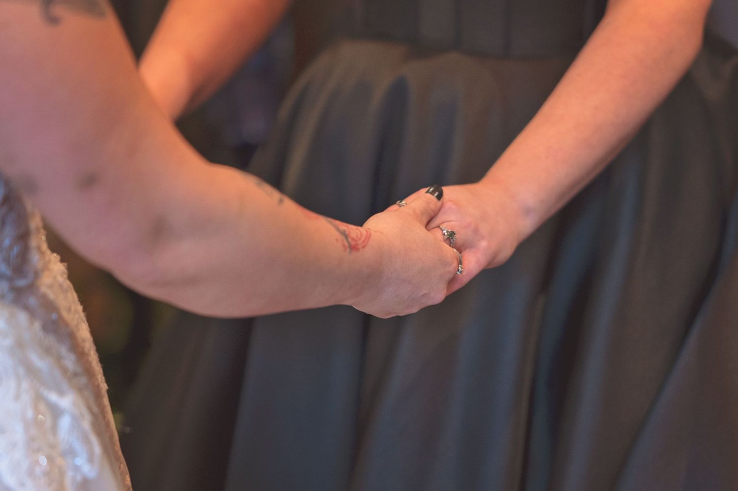 Two women hold hands, one wearing a wedding ring, in a close and intimate moment.