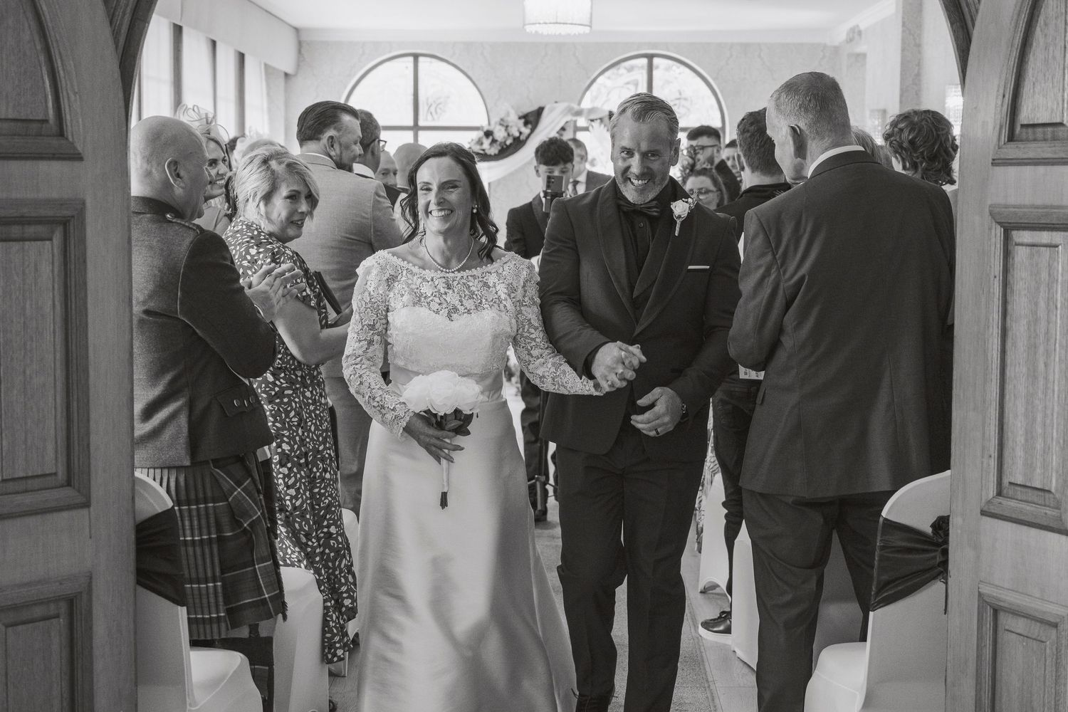 Black and white photo of a bride and groom walking down the aisle at their wedding ceremony.