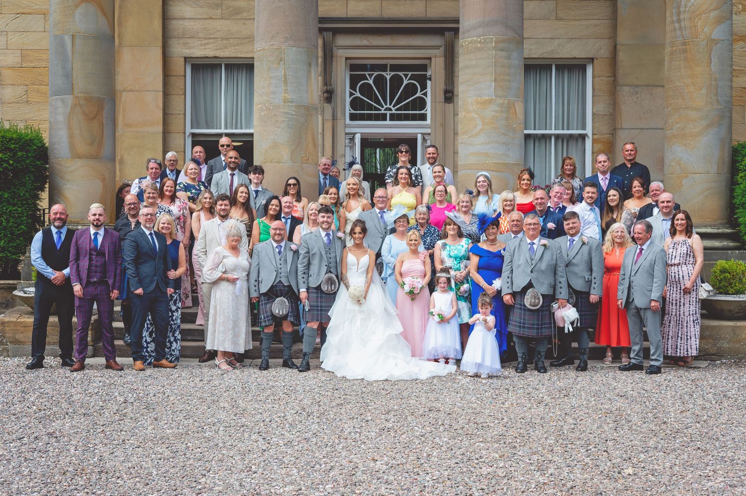 Wide angle shot of wedding guests assembled on stone steps of an elegant country estate.