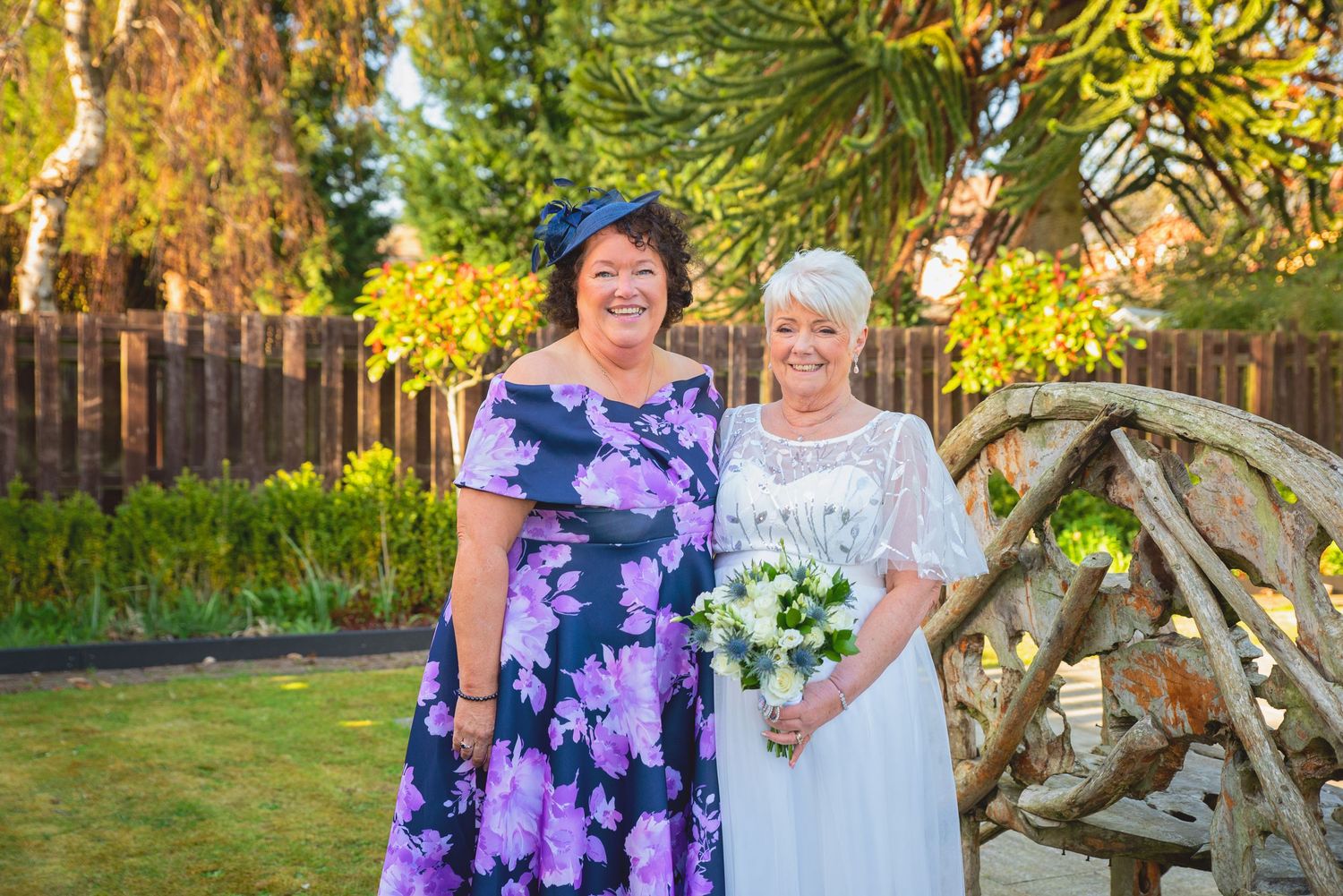 Wedding guests in colorful floral dresses pose for outdoor photos in a garden setting.