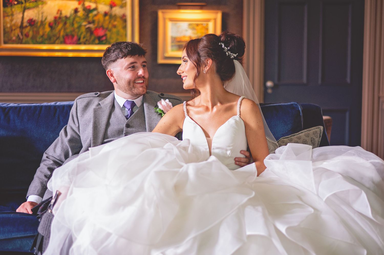 Couple shares intimate moment on elegant couch during wedding reception.