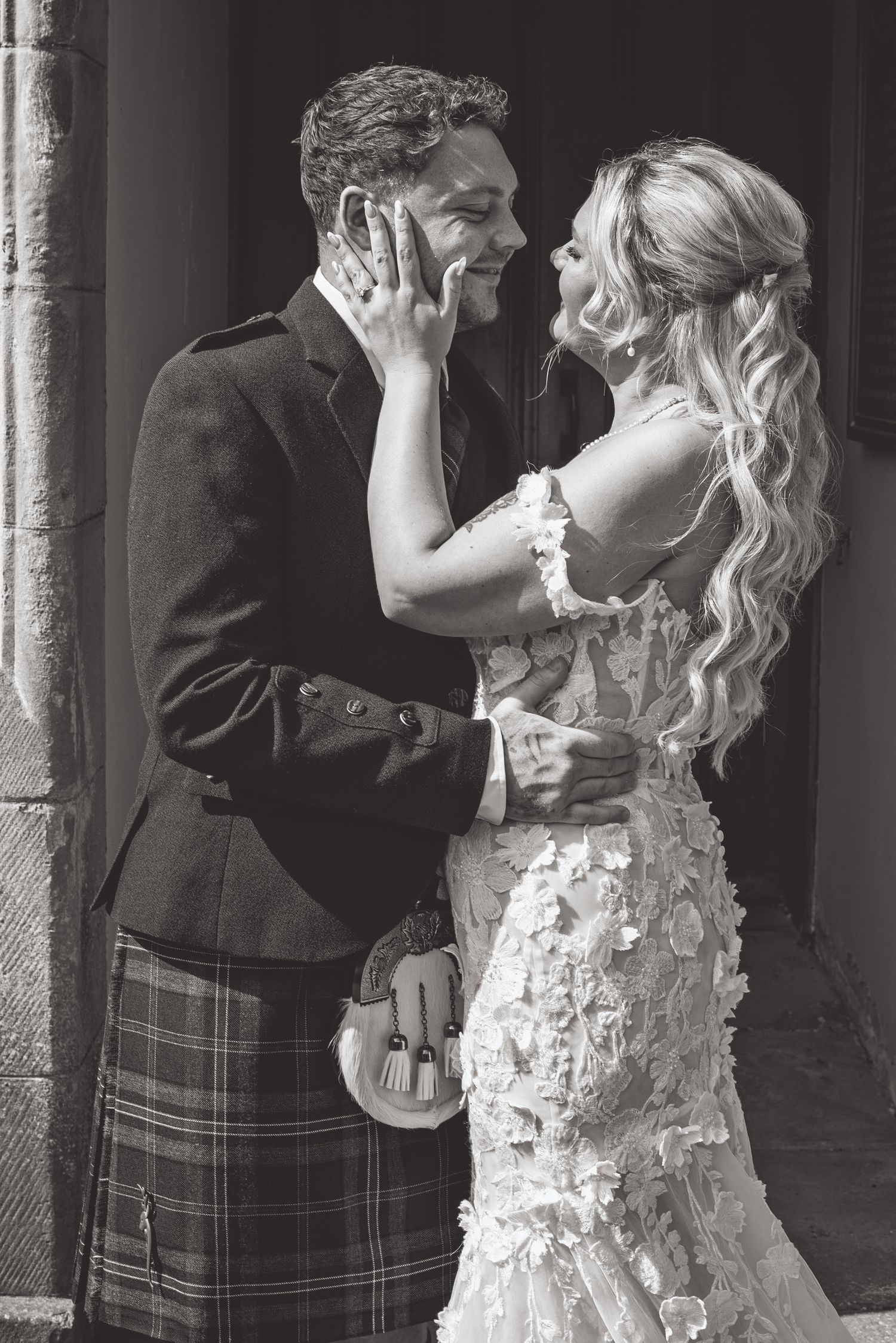 Wedding couple sharing romantic moments against stone pillars in formal attire.