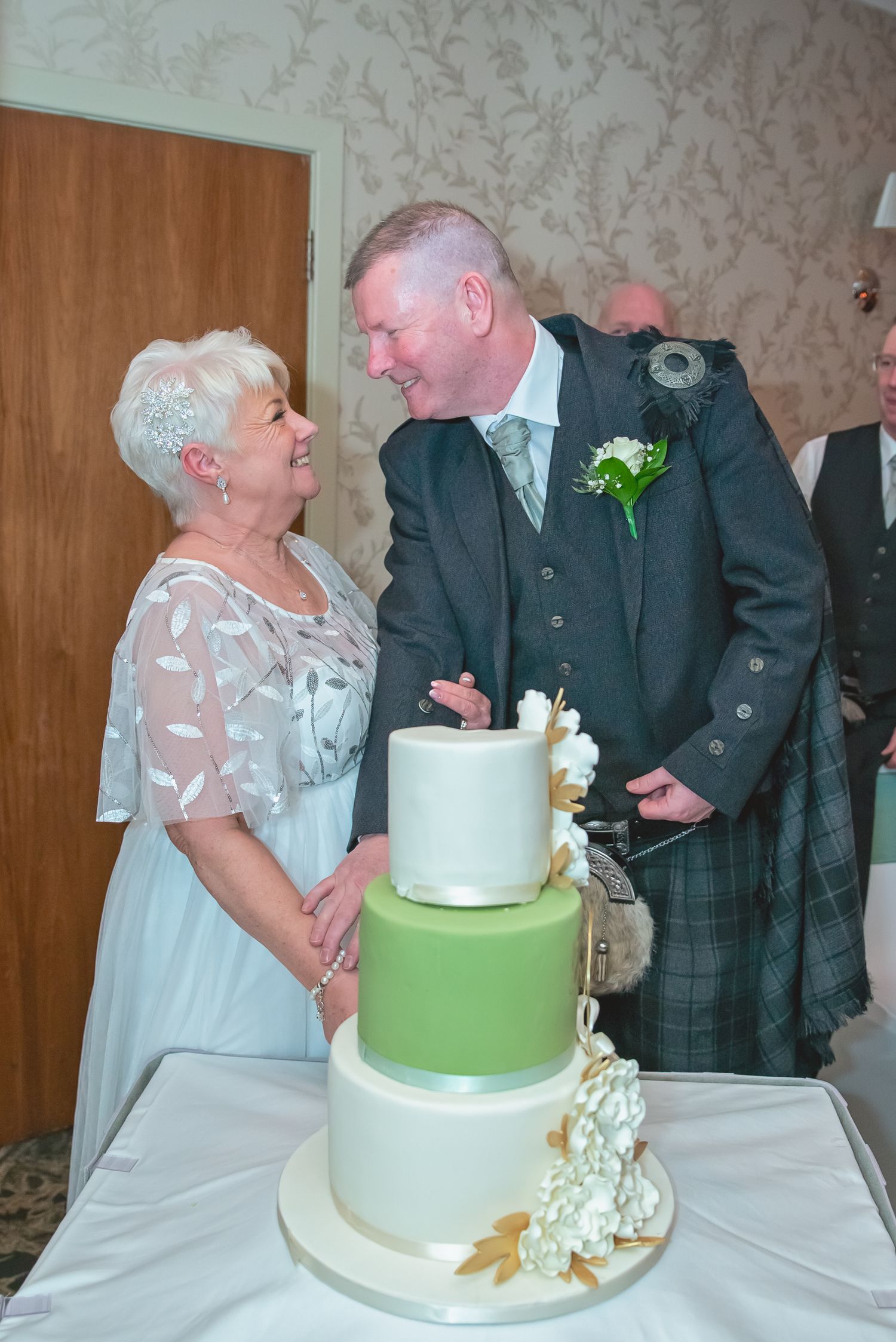 A couple stands beside their three-tiered white and green wedding cake.