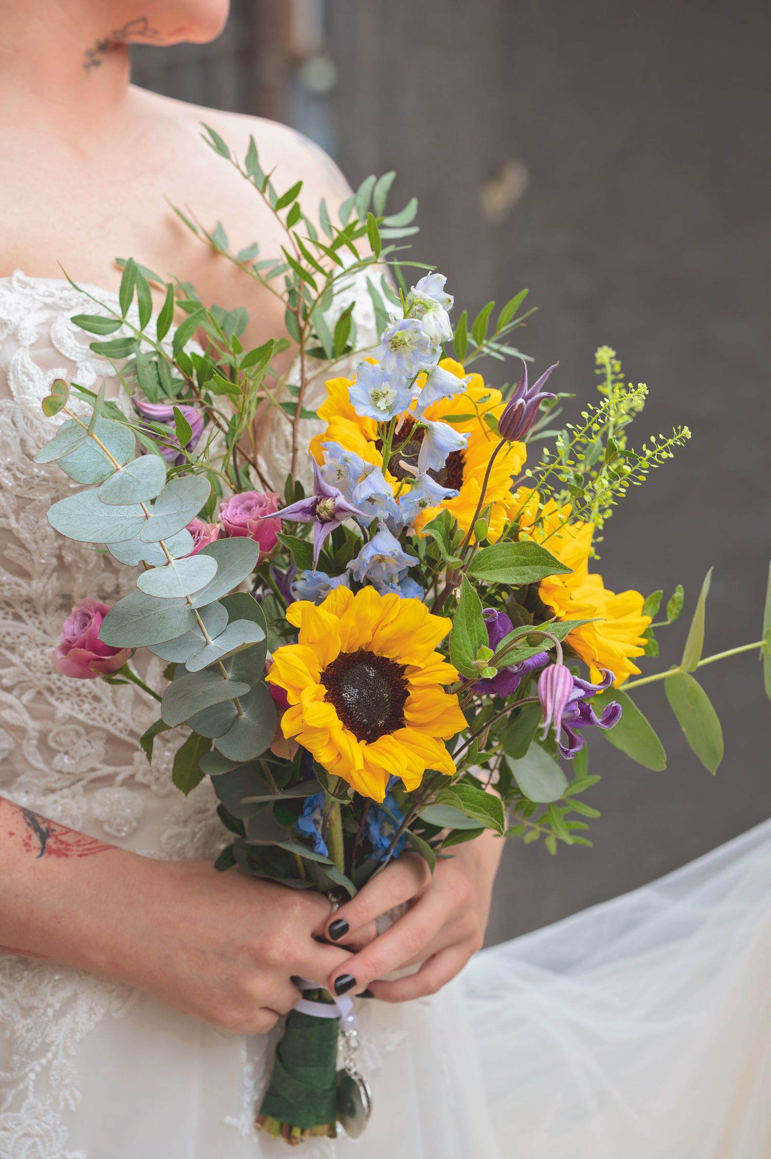 Bride holds a vibrant wedding bouquet featuring sunflowers, purple blooms, and eucalyptus greenery.