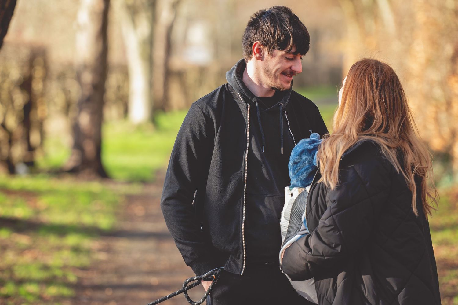 Two people having a conversation while standing on a path in a park during autumn.