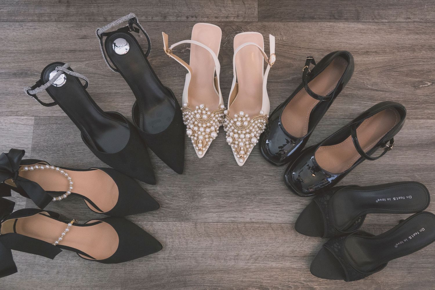 Five pairs of black and beige women's heels and flats arranged in a fan pattern on a wooden floor.
