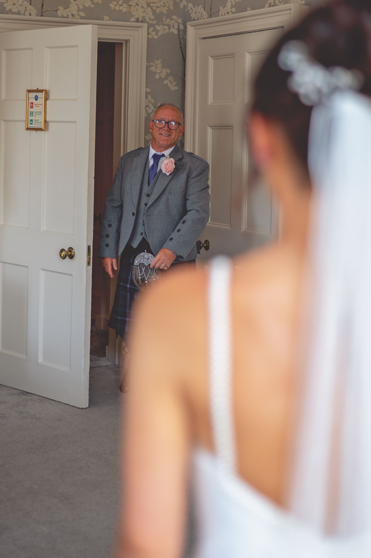 Wedding first look moment with suited guest watching bride through doorway.