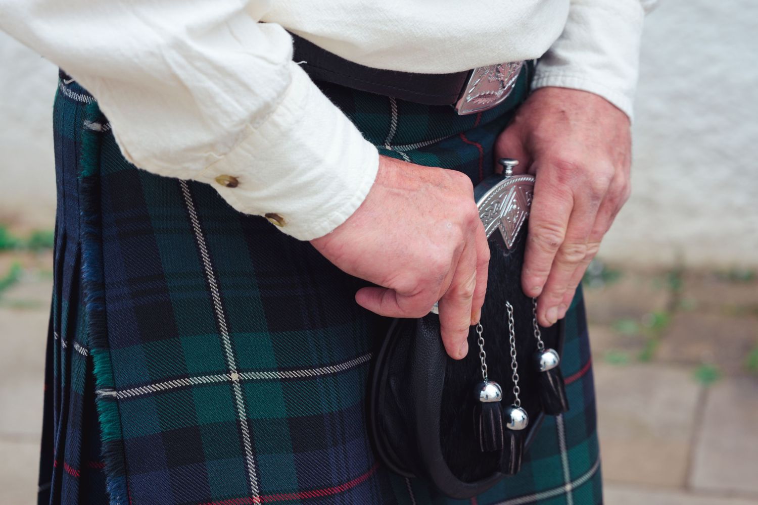 Person wearing a green tartan kilt holding a sporran with silver chains at a Scottish event.