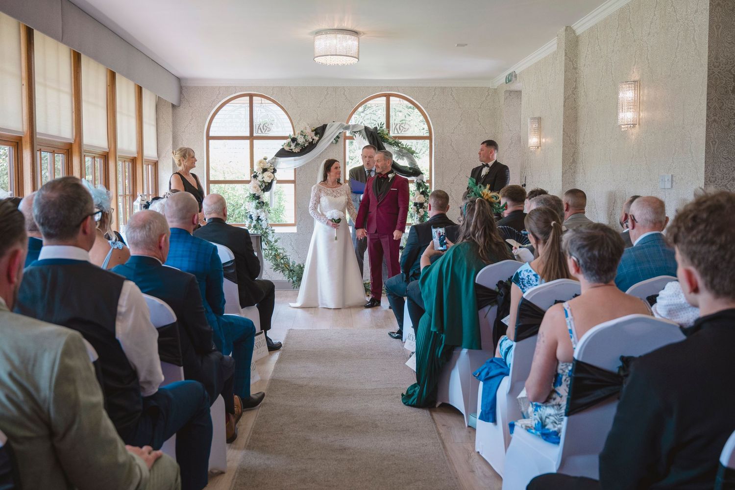 Elegant wedding ceremony in a bright venue with guests seated as couple exchanges vows before an officiant.