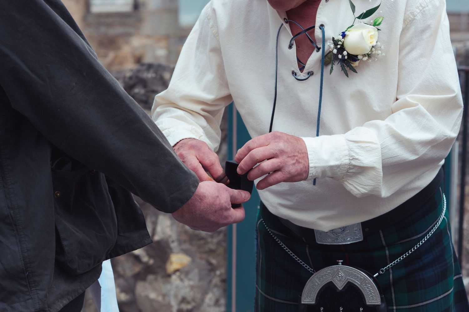 Man in Scottish kilt and white shirt with boutonniere exchanges rings during outdoor wedding ceremony.