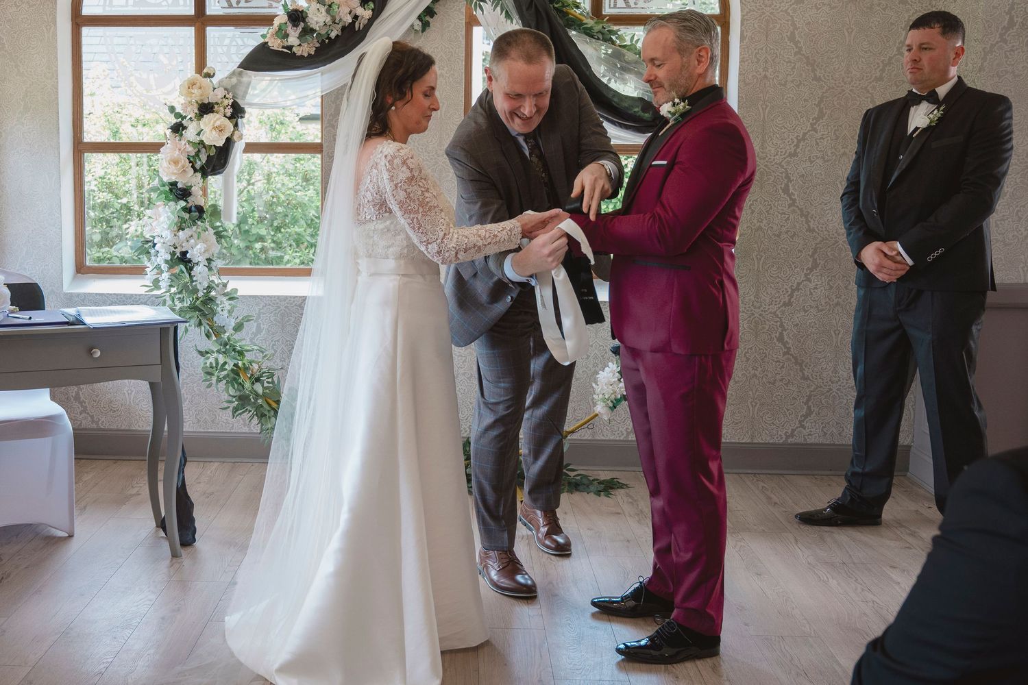 Bride and groom exchange vows during wedding ceremony with officiant performing handfasting ritual in elegant venue.