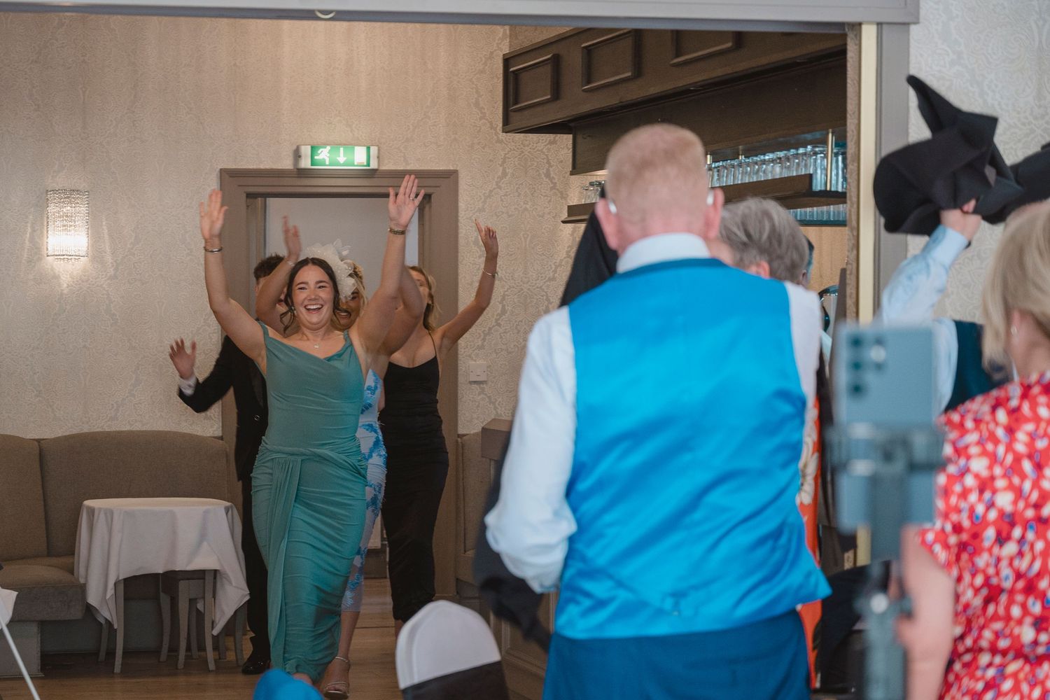 Guests dancing and celebrating at a wedding reception in an elegant venue with a man in a blue waistcoat.