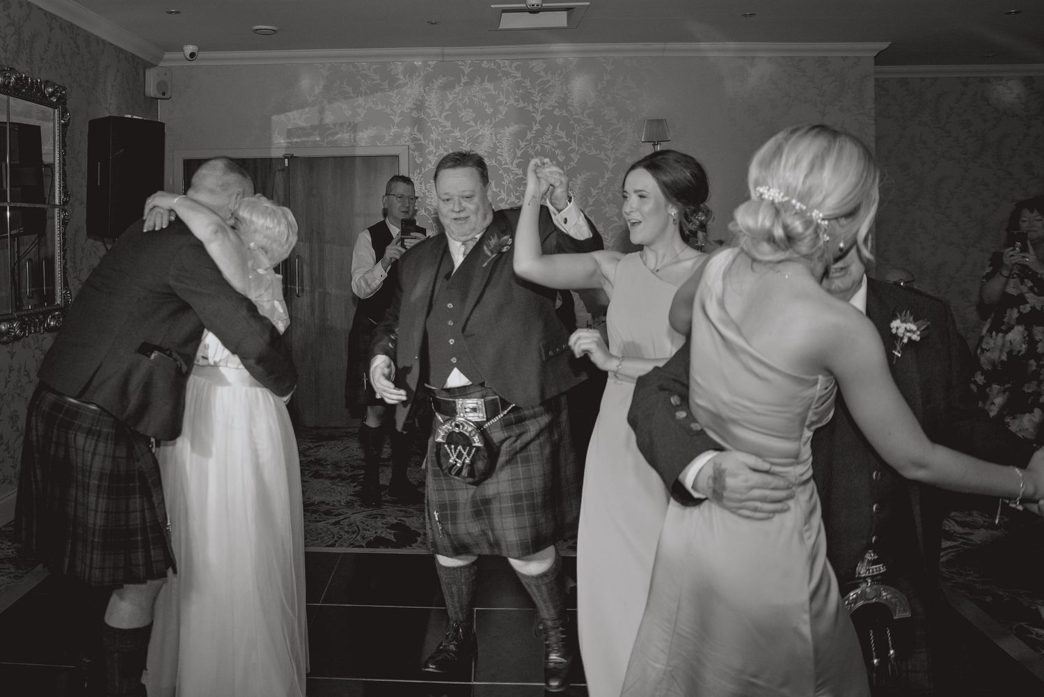Wedding guests dancing and celebrating on a dimly lit dance floor.