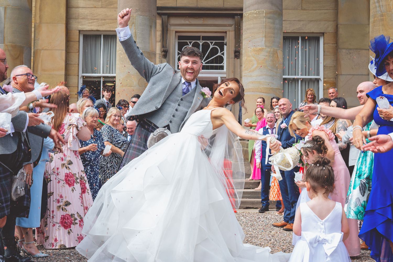 Large group photo of wedding guests gathered outside a grand stone building for a formal celebration.