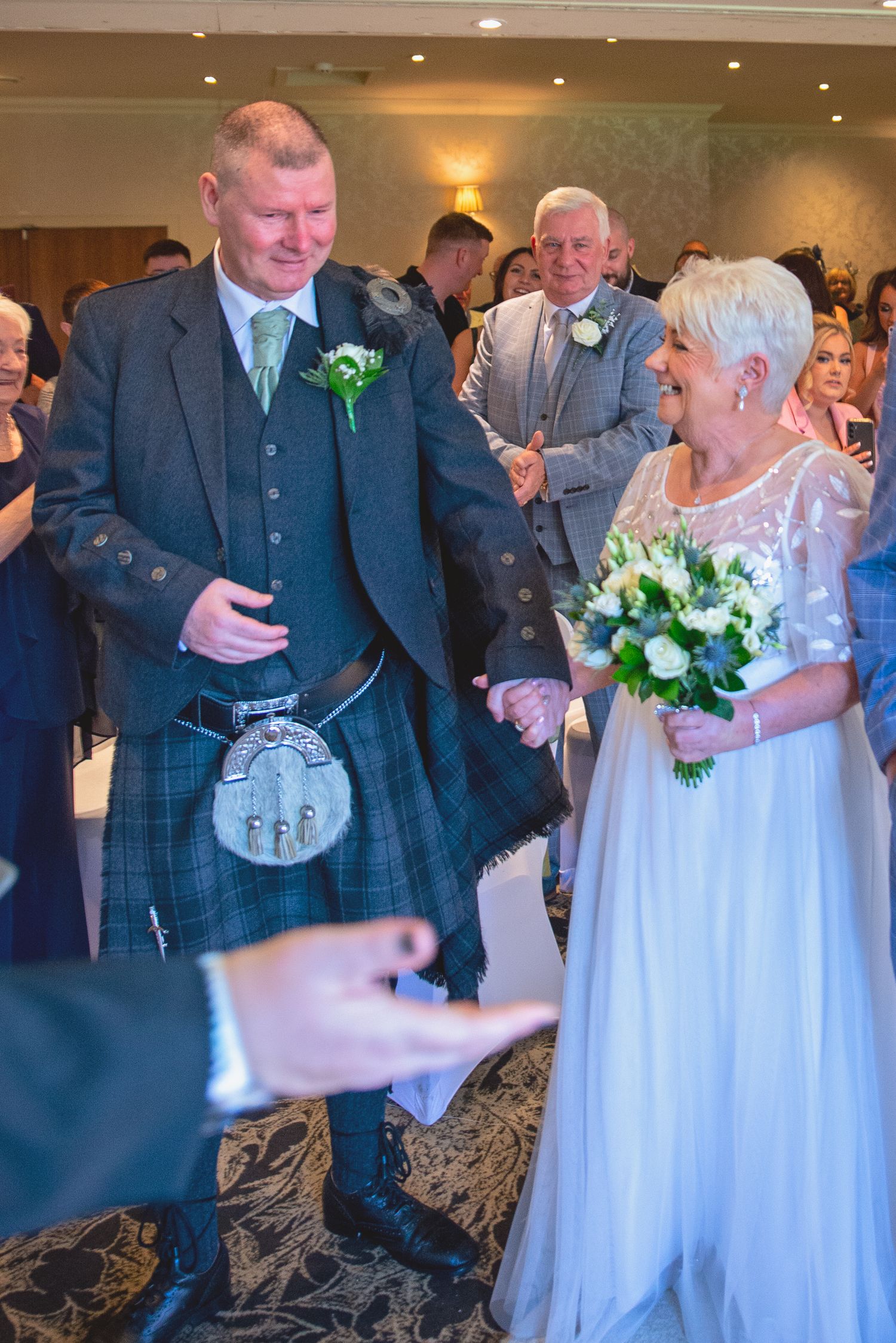 Wedding party members in Scottish attire and white gowns celebrate during a reception.