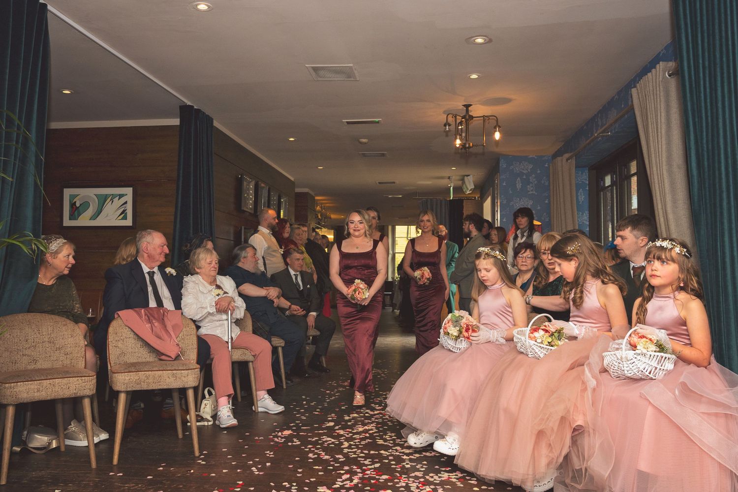 Wedding processional with flower girls in pink dresses walking down the aisle past seated guests.