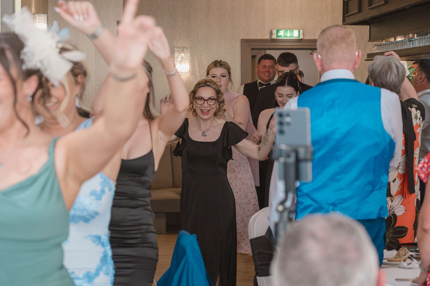 Guests dancing joyfully at a wedding reception in a decorated venue, with women in elegant dresses celebrating on the dance floor.