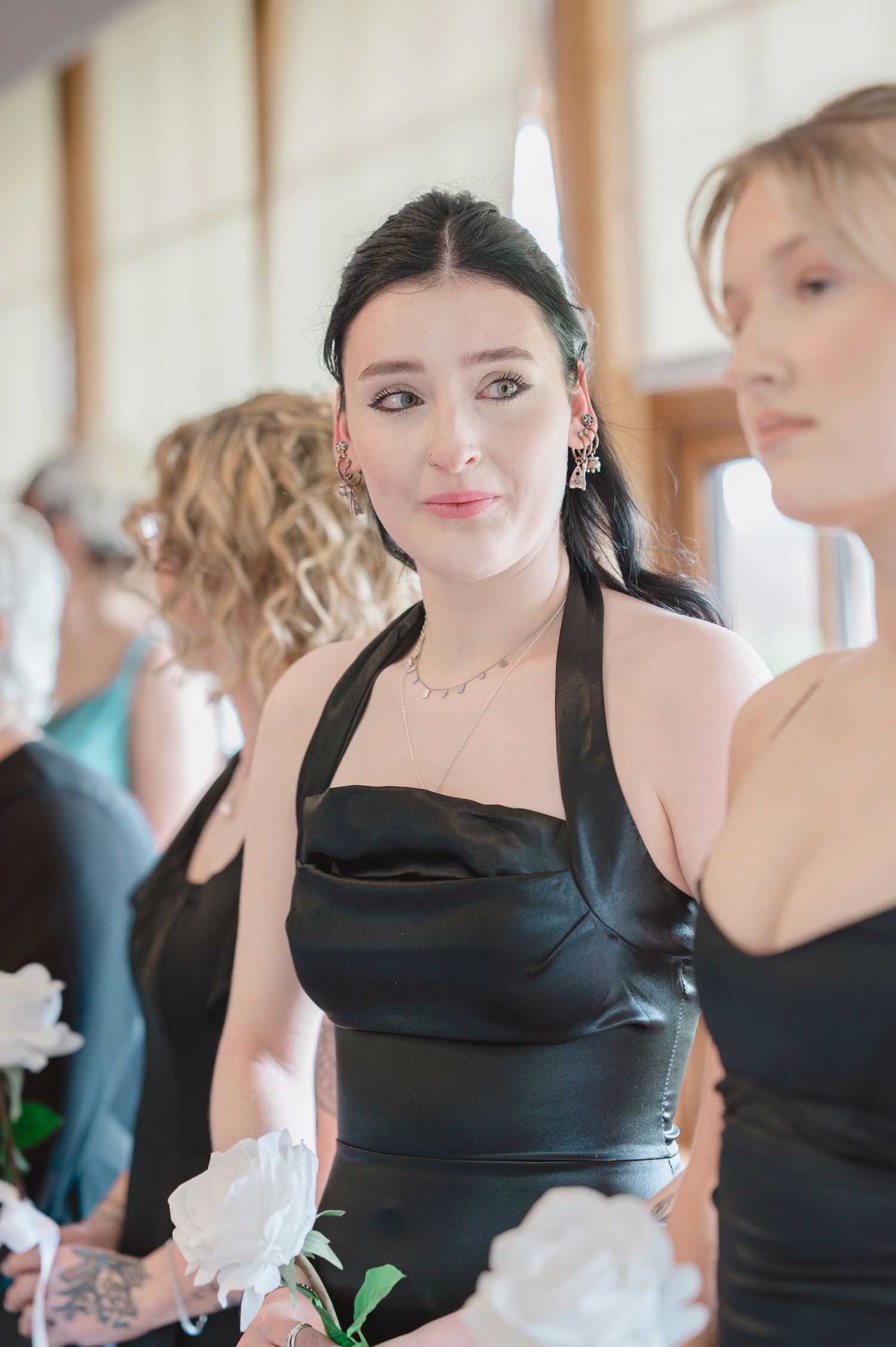 Woman in black satin halter dress holding white rose at a wedding ceremony.