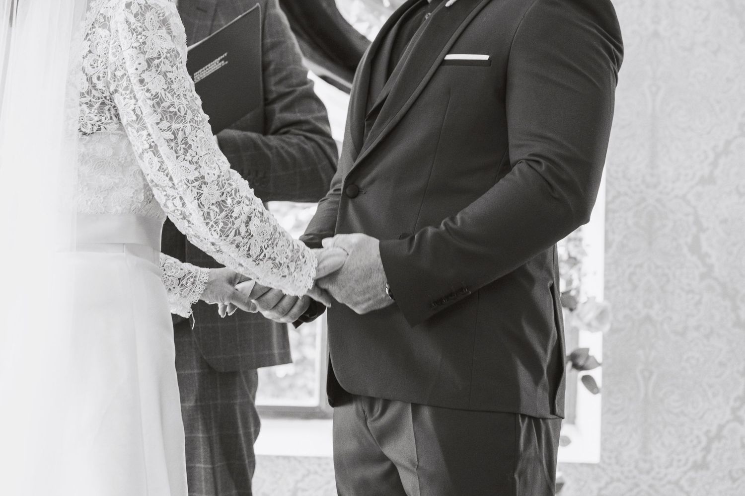 Black and white wedding photo of groom placing ring on bride's finger during ceremony.