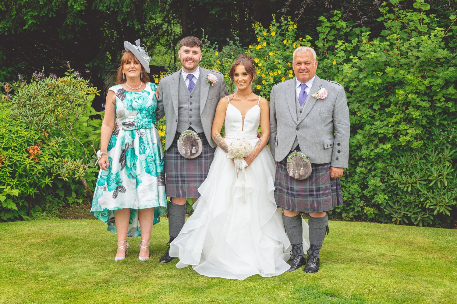 Wedding party in Scottish formal wear poses together on garden lawn.