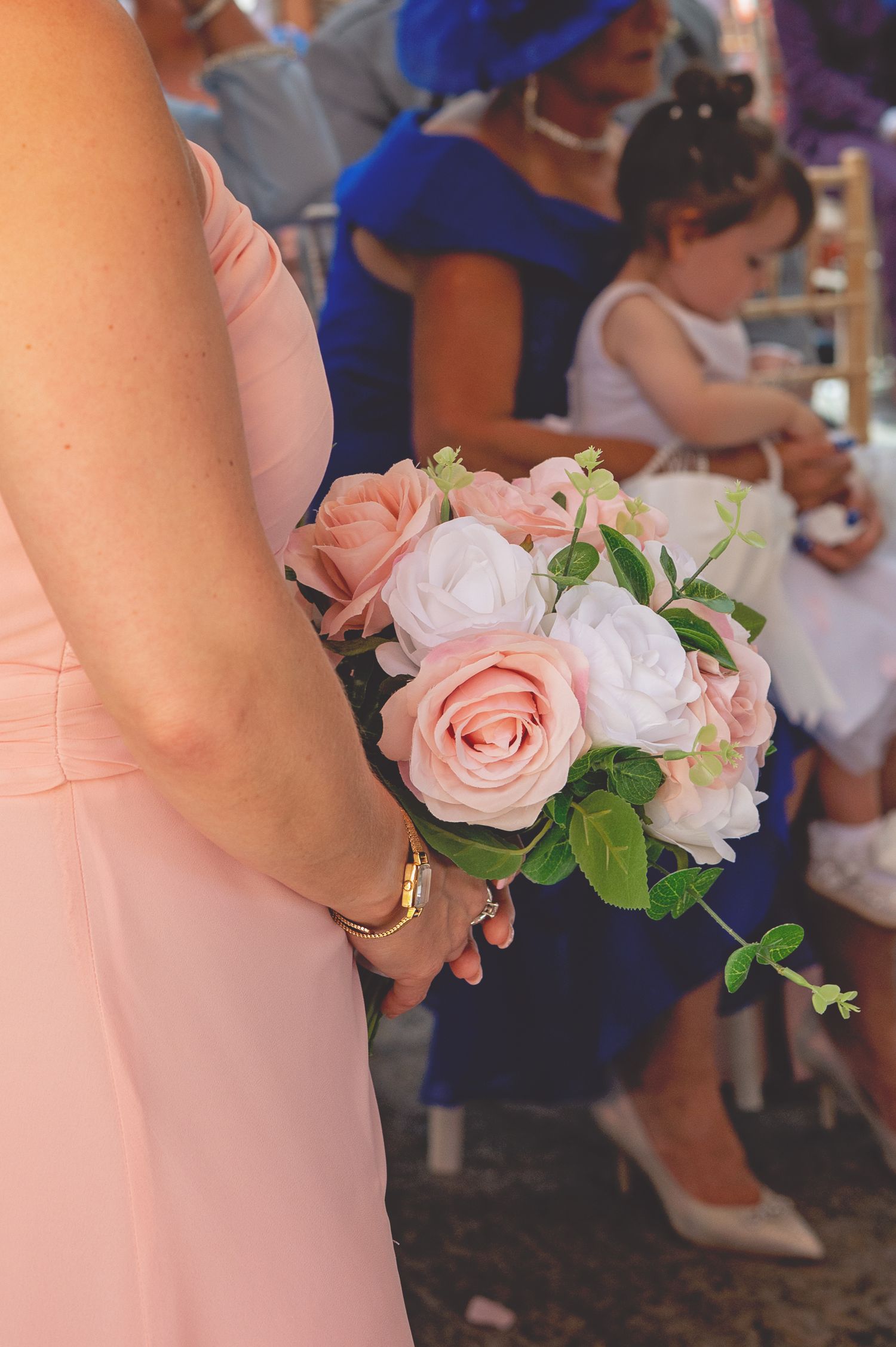 A bridesmaid in a pink dress holds a delicate bouquet of pink and white roses.