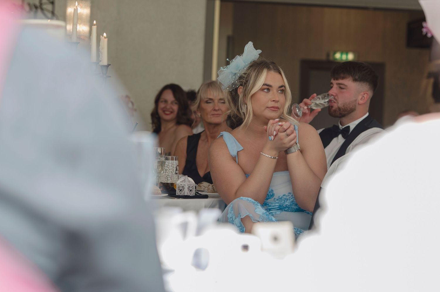 Elegantly dressed guests at a formal wedding reception, woman in blue dress with fascinator hat.