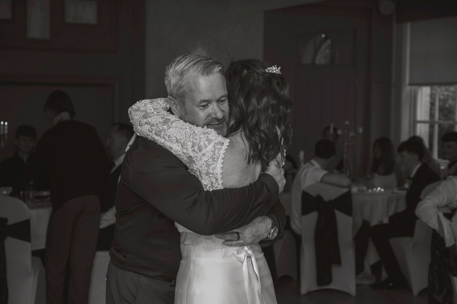 Black and white photo of bride and groom sharing emotional embrace during first dance at wedding.