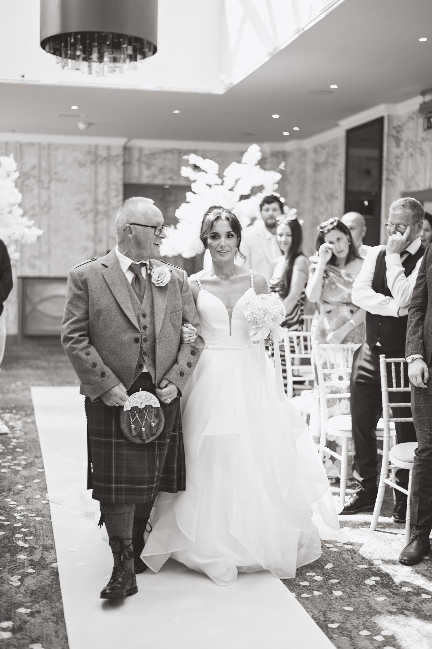 Black and white photo of a traditional Scottish wedding ceremony with white floral decorations.