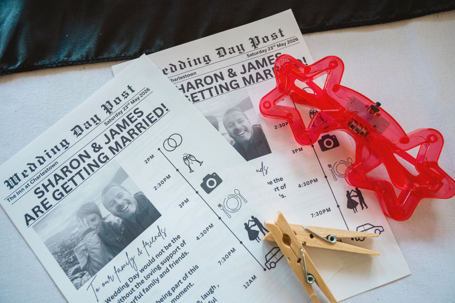 Wedding Day Post newspaper programs for Sharon and James with red star glasses and wooden clothespins on white surface.