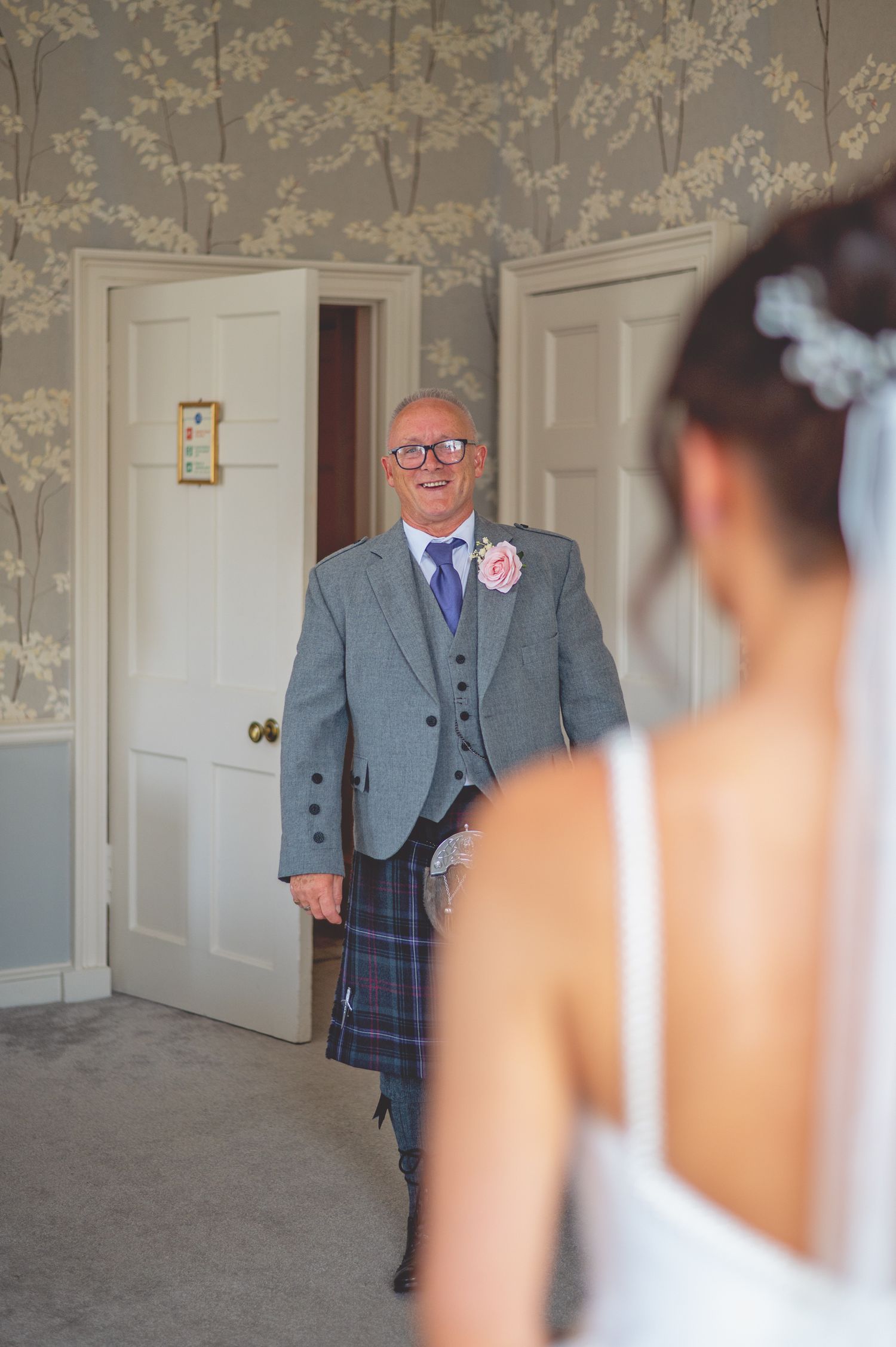 Wedding scene in an elegant room with floral wallpaper and white doors.