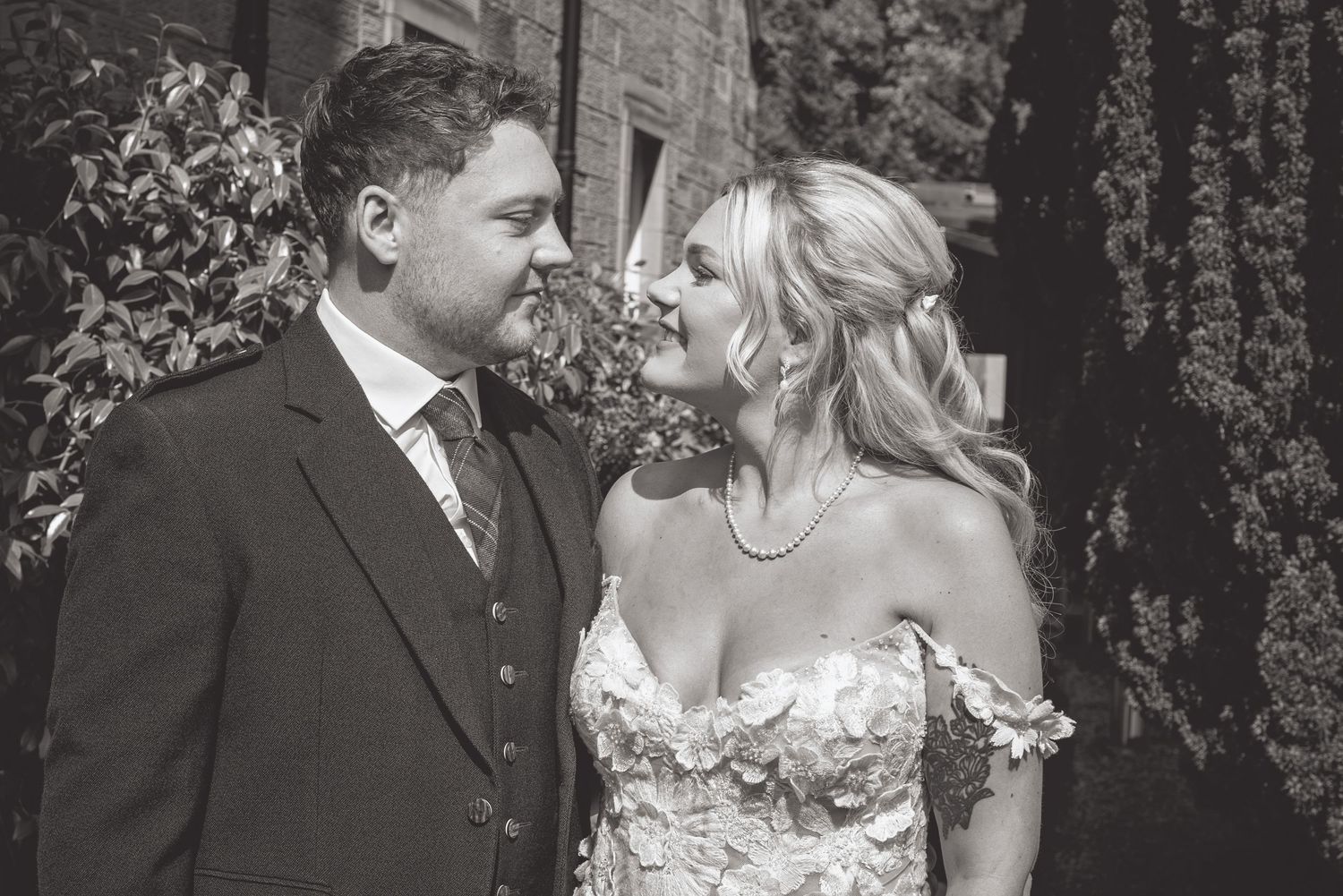 Romantic wedding couple sharing intimate moments in a garden setting with stone architecture.