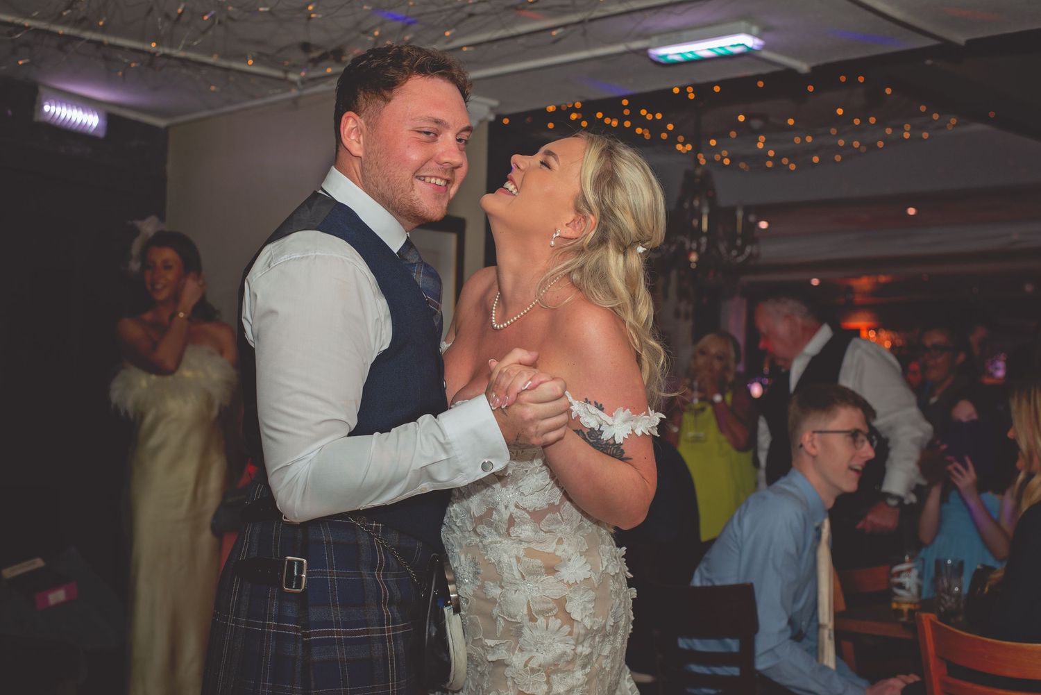 Wedding couple shares their first dance on a dimly lit dance floor with string lights overhead.