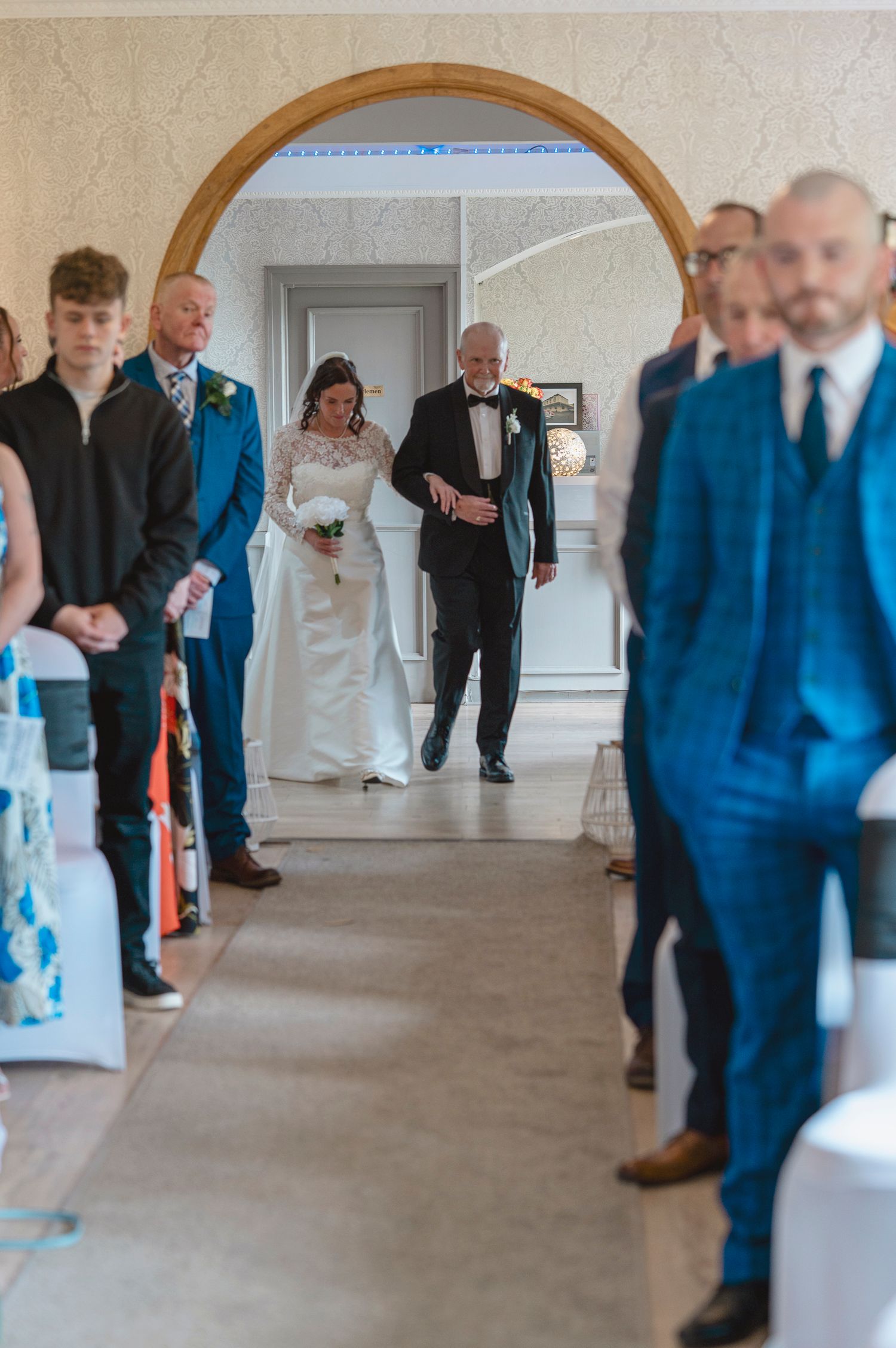 Bride walks down the aisle with escort through an archway at an elegant wedding ceremony.