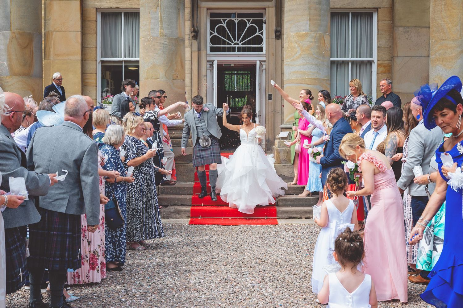 Wedding party and guests gather outside an elegant stone venue.