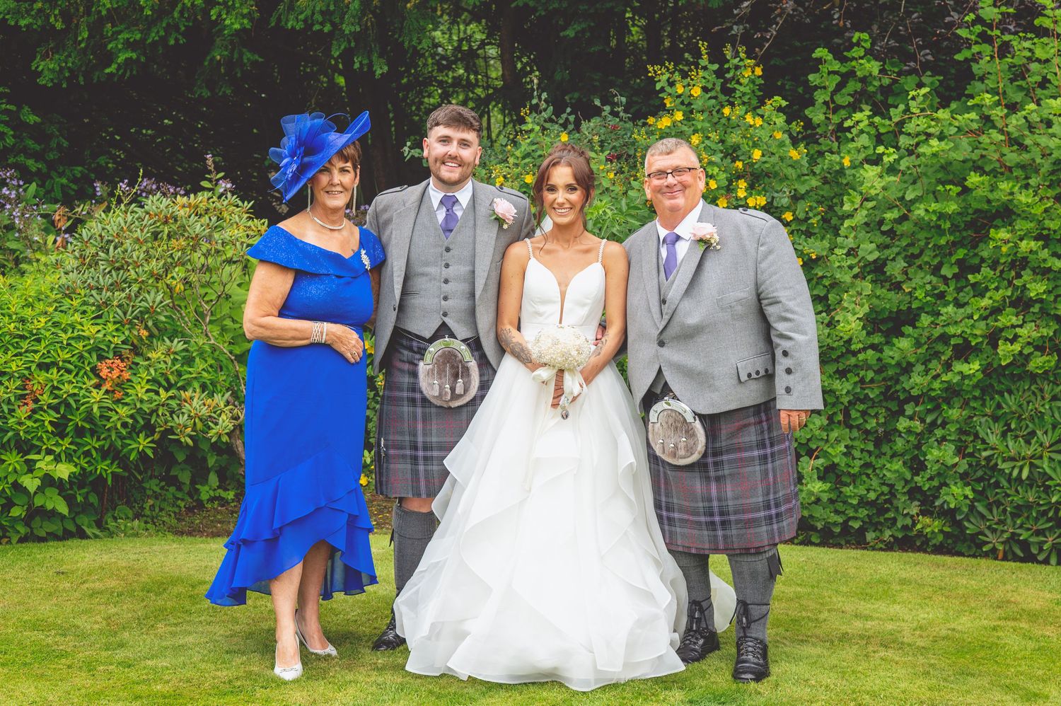 Wedding party in grey suits and blue dresses pose together in a garden setting.