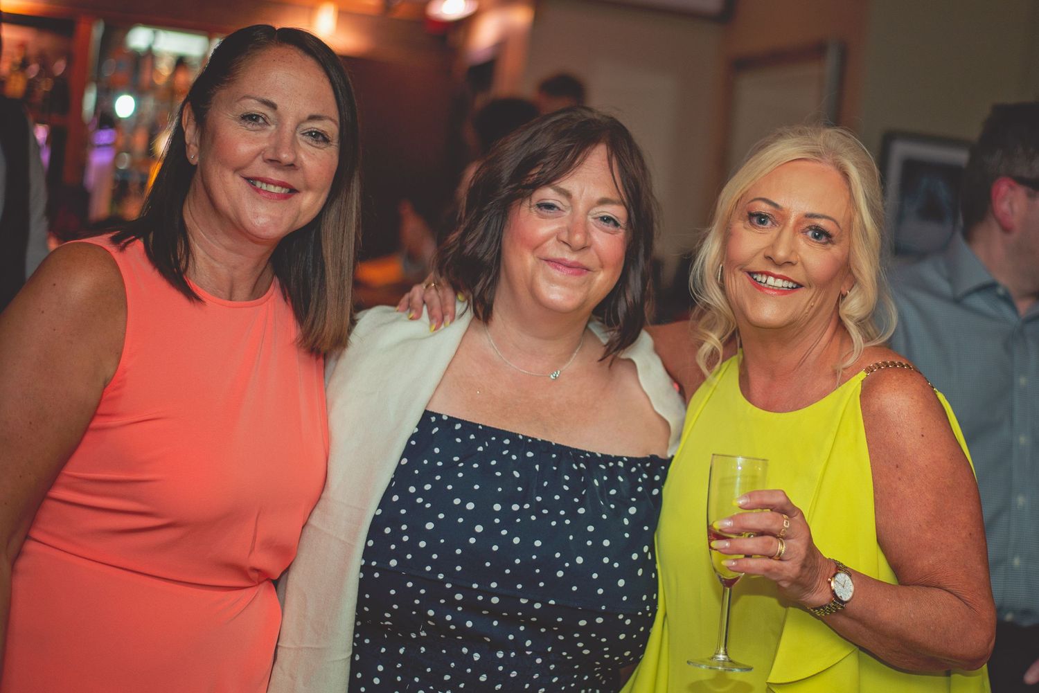 Three wedding guests in bright colored dresses smiling at a reception party.