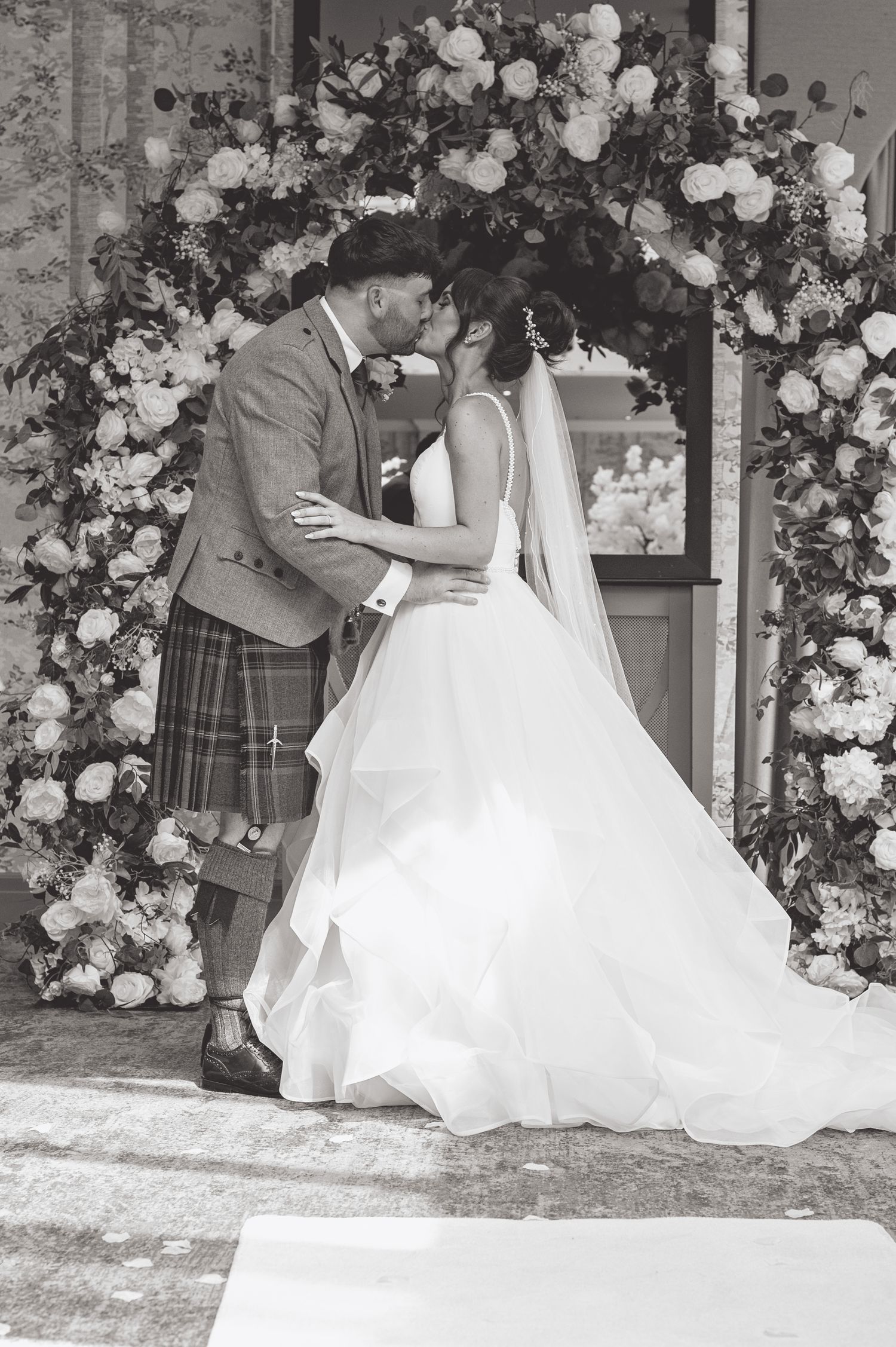 Newlyweds pose under floral arch during romantic wedding photoshoot.